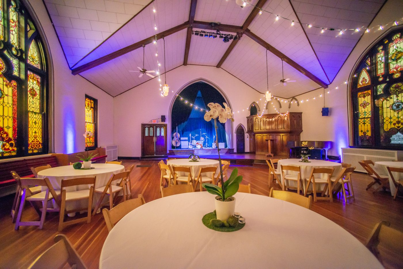 The Sanctuary under violet uplighting and café lights, set with round tables facing the stage